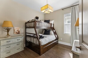 A bunk bed with a ladder, a dresser, a lamp, and a window with blinds.