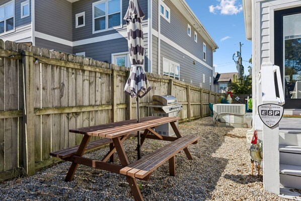 A picnic table with benches, a grill, and a wooden fence in a backyard.
