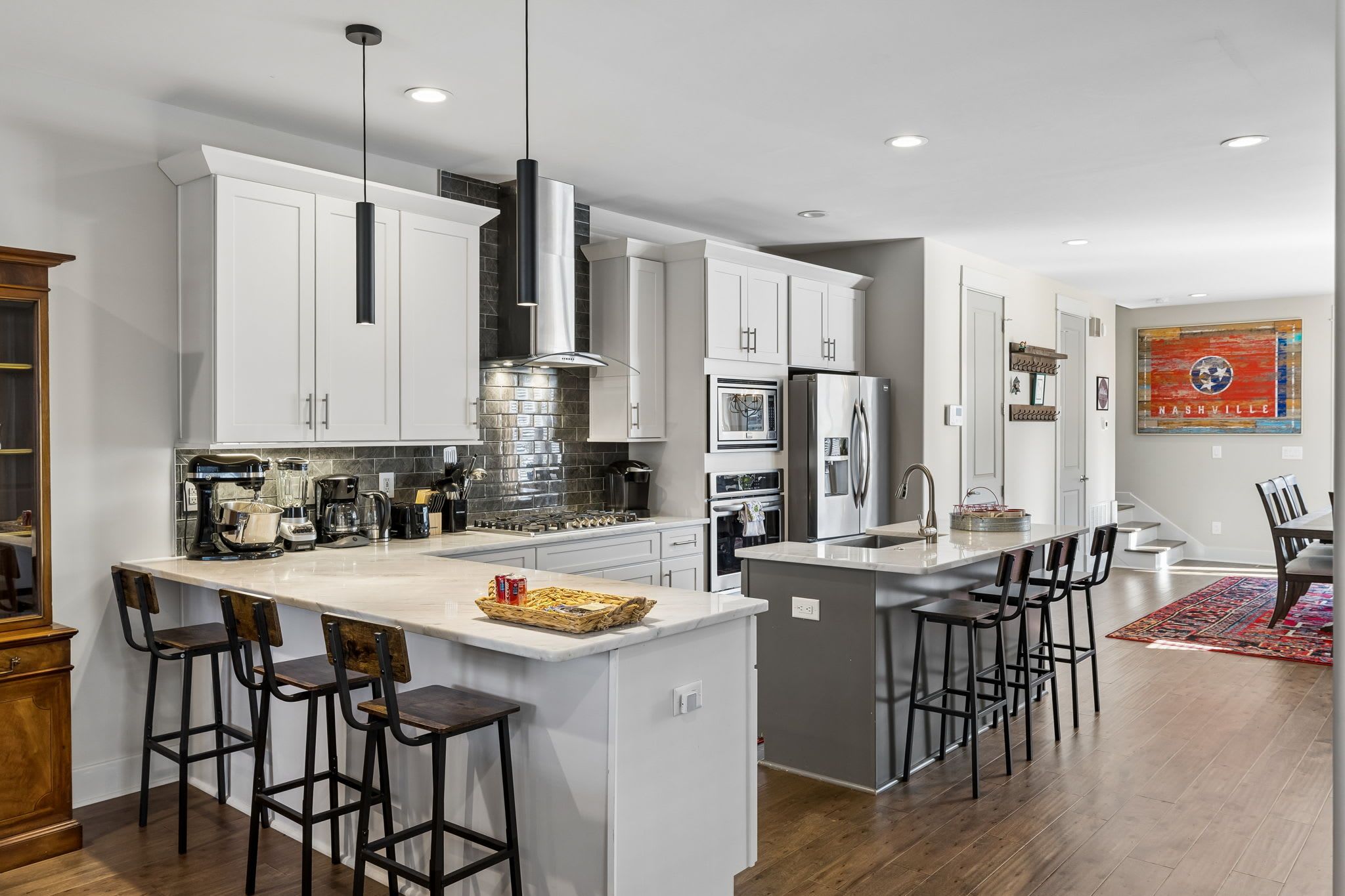 A modern kitchen with white cabinets, stainless steel appliances, and a central island with bar stools.