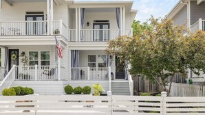 A two-story white house with a front porch, a small garden, and a wooden fence.