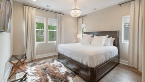 A bedroom with a large bed, a chandelier, and a view of the outdoors through the windows.