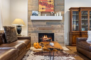 A living room with a fireplace, leather sofas, a coffee table, and a wooden wall with a Nashville sign.