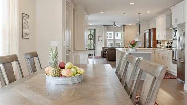 A spacious dining area with a wooden table and chairs, a fruit bowl, and a modern kitchen in the background.