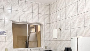 A modern kitchen with white marble tiles, a black countertop, a sink, a stove, a coffee maker, and three potted plants. - Condomínio Gelatti (Ubatuba)