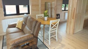 A wooden cabin interior with a brown leather sofa, a dining table with chairs, and a potted plant.