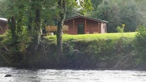 A cabin with a wooden exterior, situated beside a river. - #2 Killarney Cabins, Stunning Lodge & Parking (Killarney)
