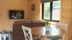 A cozy cabin interior with a wooden ceiling, a sofa, a dining table with chairs, and a television mounted on the wall. - #2 Killarney Cabins, Stunning Lodge & Parking (Killarney)