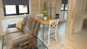 A wooden cabin interior with a brown leather sofa, a wooden dining table, white chairs, a potted plant, and a remote control on a small table. - #2 Killarney Cabins, Stunning Lodge & Parking (Killarney)