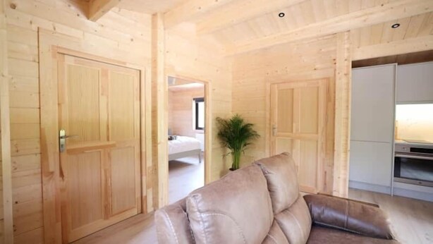 A wooden interior with a sofa, a plant, and a bed in the background. - #2 Killarney Cabins, Stunning Lodge & Parking (Killarney)