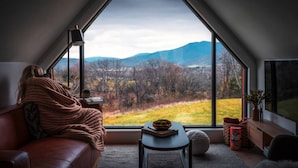 A cozy room with a large window offering a view of a mountainous landscape. - Modern A-Frame w/ Hot Tub, Sauna & Stunning Views (Stanley)