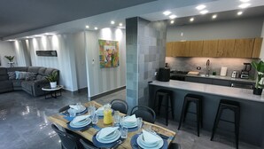 Een moderne keuken met een centraal eiland, barkrukken en een eethoek met een houten tafel gedekt voor vier personen.