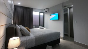 Een moderne hotelkamer met een groot bed, een flatscreen televisie aan de muur, een nachtkastje met een lamp en uitzicht op een strand door het raam.