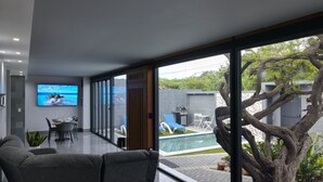 Een moderne woonkamer met een grote televisie, een eethoek en uitzicht op een zwembad.