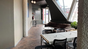 A modern interior with a high ceiling, exposed beams, and a mix of seating areas including a sofa and tables. - Blue Hostel Bláu Fjöll (Vestmannaeyjar)