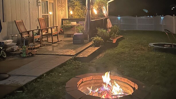 A backyard with a fire pit, outdoor seating, and string lights.