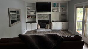 A living room with a fireplace, white cabinets, a flat-screen TV, and a large window.