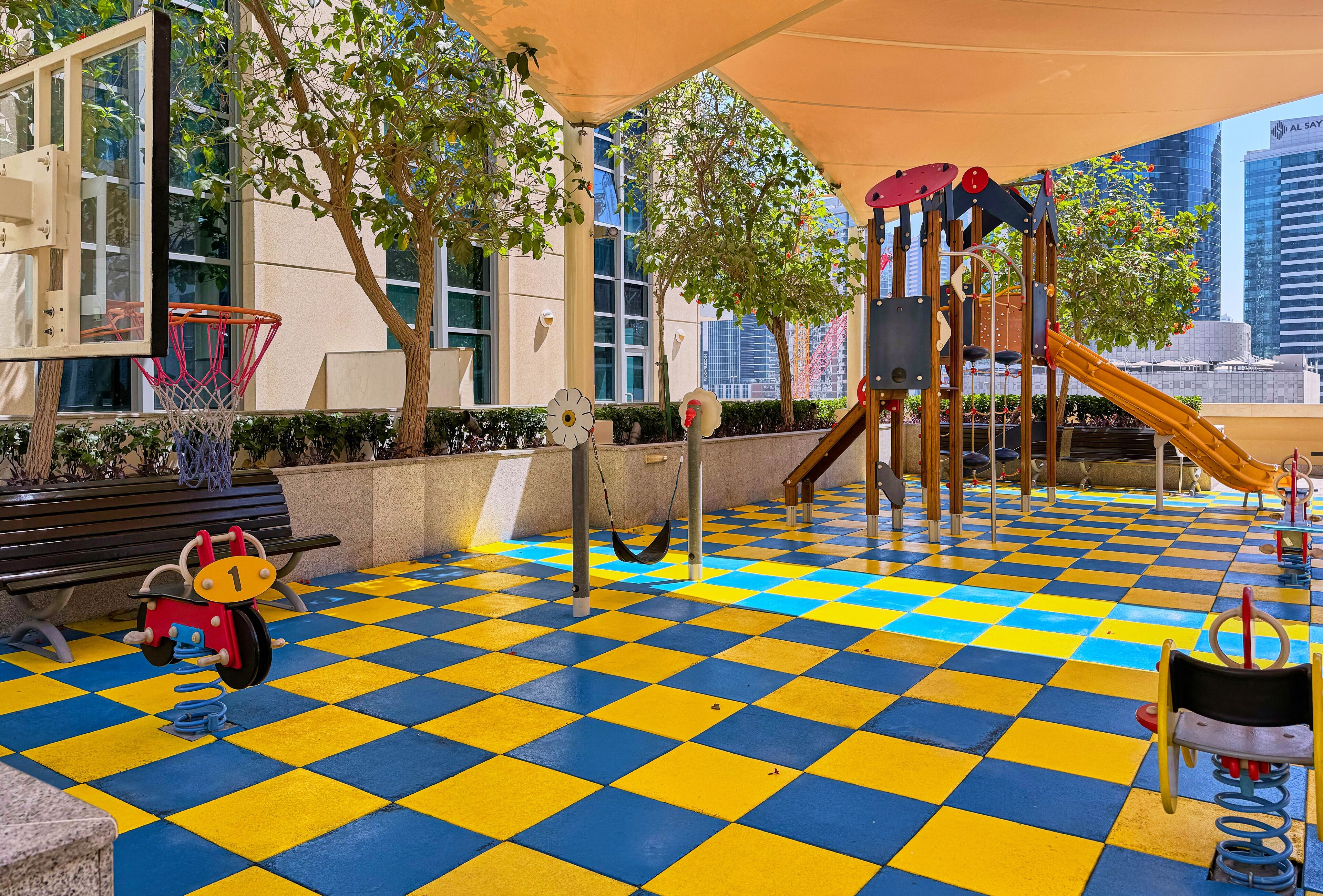 A playground with a checkered floor, a basketball hoop, and a swing set.