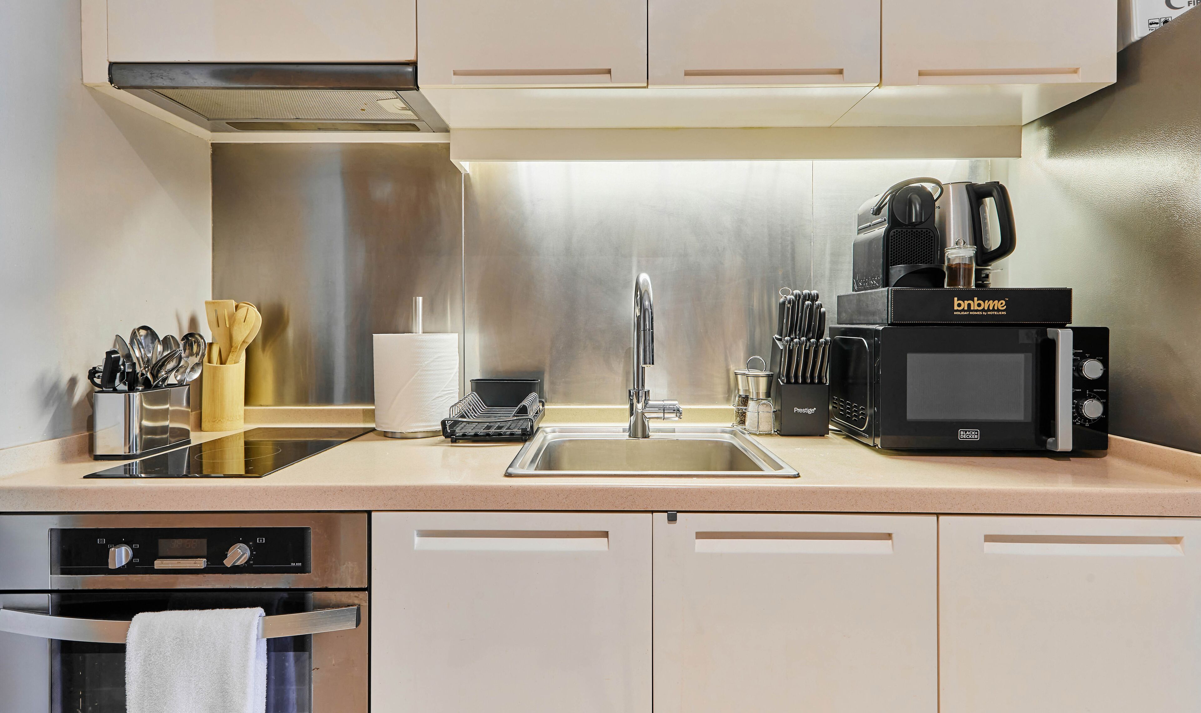 Une cuisine moderne équipée d’un évier en acier inoxydable, d’une machine à café noire, d’un four à micro-ondes et d’un ensemble de couteaux.
