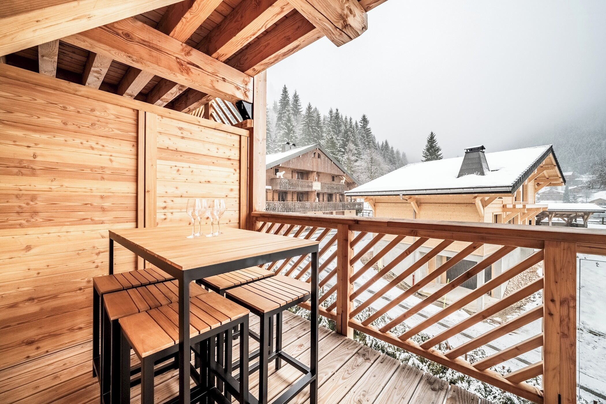 A wooden deck with a table and benches, overlooking a snowy mountain landscape.