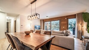 A modern living room with a wooden dining table, a sofa, and a large window with a view of trees. - Ubuntu - Stylish Alpine Apartment in Châtel (Châtel)