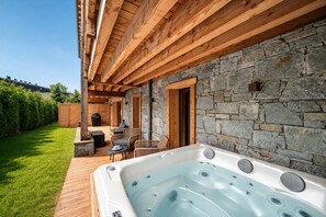 A wooden deck with a hot tub, stone walls, and outdoor furniture.