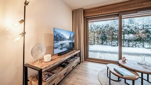 A modern living room with a television, wooden furniture, and a large window offering a view of a snowy landscape. - Ubuntu - Stylish Alpine Apartment in Châtel (Châtel)