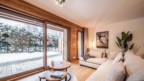 A modern living room with a large window, a wooden deck, a sofa, and a coffee table. - Ubuntu - Stylish Alpine Apartment in Châtel (Châtel)