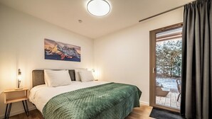 A modern bedroom with a large bed, a nightstand, a painting, and a view of a snowy outdoor area. - Ubuntu - Stylish Alpine Apartment in Châtel (Châtel)