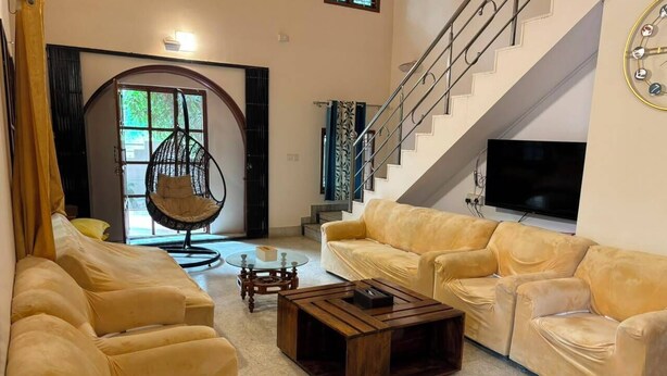 Una sala de estar con un sofá, una mesa de centro, un sillón colgante, una escalera y un televisor.