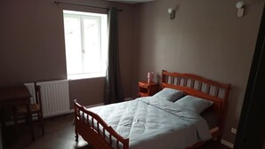 Une chambre à coucher avec un lit en bois, une table de chevet, une chaise, une fenêtre avec des rideaux et un radiateur.