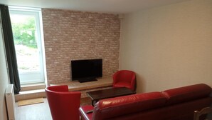 Un salon avec un mur en briques, un téléviseur à écran plat, un canapé en cuir rouge et un fauteuil rouge.