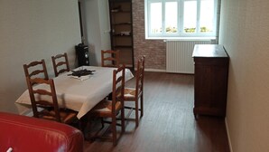 Un coin repas avec une table et des chaises, une bibliothèque, un radiateur et une fenêtre donnant sur un paysage verdoyant.