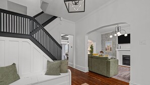 A modern living room with a staircase, a fireplace, and a green sofa. - Family Getaway with Backyard + Games: Near Downtown St. Louis (St. Louis)