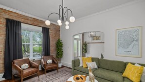 Un salon avec un mur en briques, des fauteuils en cuir, un canapé vert, une table basse et une carte accrochée au mur.