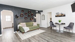 Ein modernes Wohnzimmer mit einem grünen Sofa, zwei grauen Sessel, einem runden Tisch und einer grauen Wand mit sechseckigen Regalen.