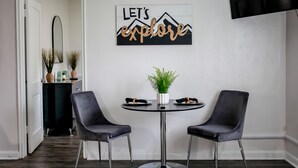 Ein Essbereich mit einem runden Tisch, zwei Stühlen, einer Topfpflanze und einem an der Wand befestigten Schild mit der Aufschrift 'LET'S explore'.