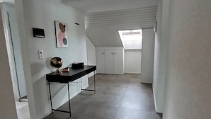 Une pièce spacieuse avec un bureau noir, des armoires blanches et un sol carrelé.