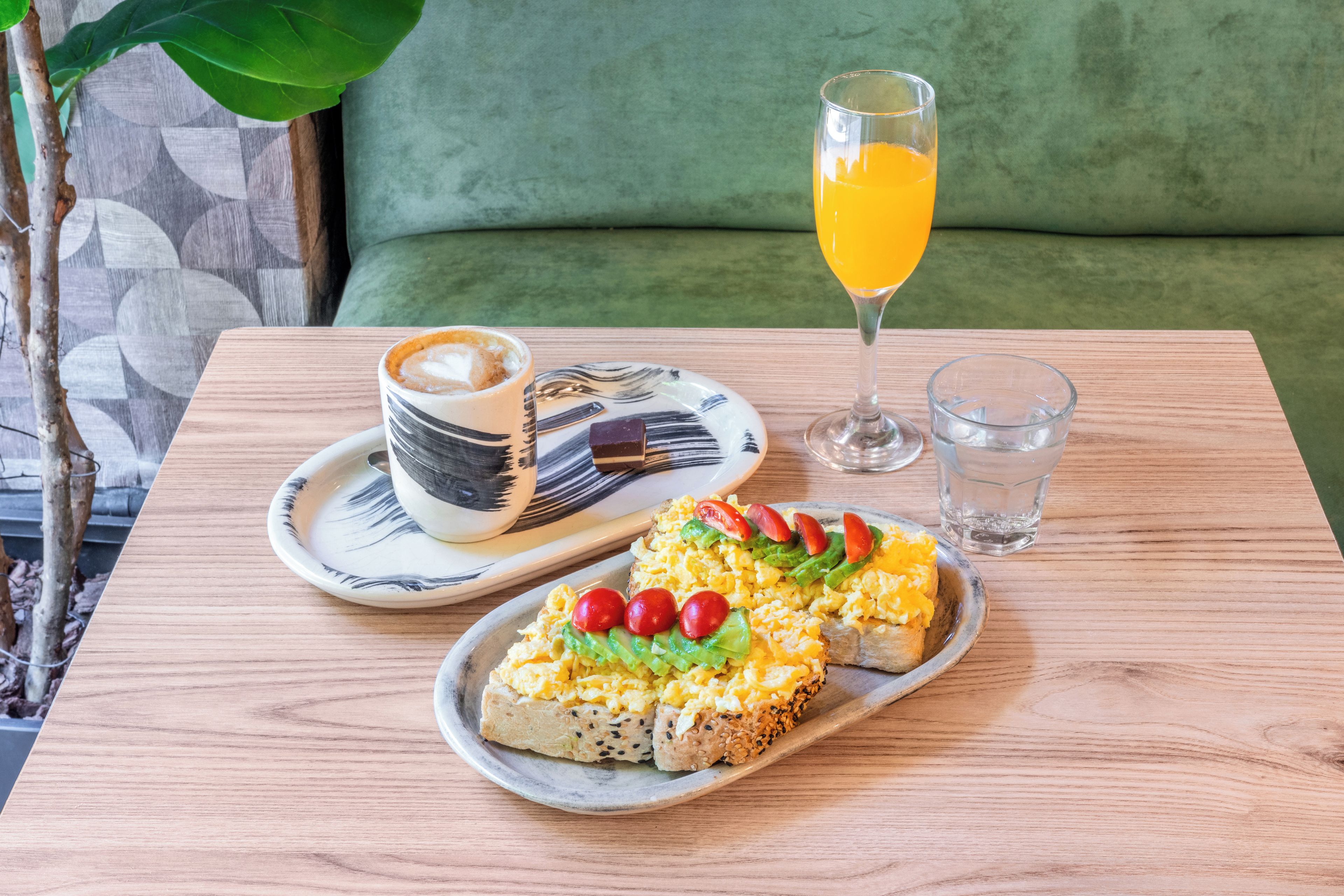 A breakfast setting with a plate of scrambled eggs, toast, and cherry tomatoes, a cup of coffee, and a glass of orange juice on a wooden table.
