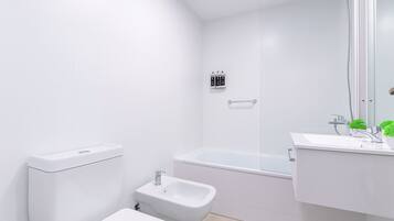 A modern bathroom with a toilet, bidet, bathtub, and a sink with a mirror.