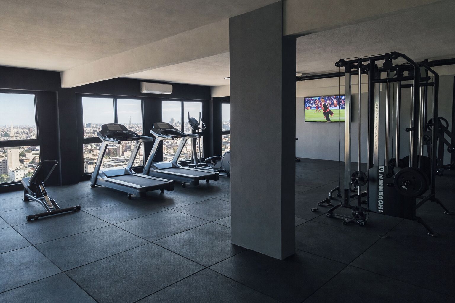 A gym with treadmills, a squat rack, and a TV displaying a sports event.