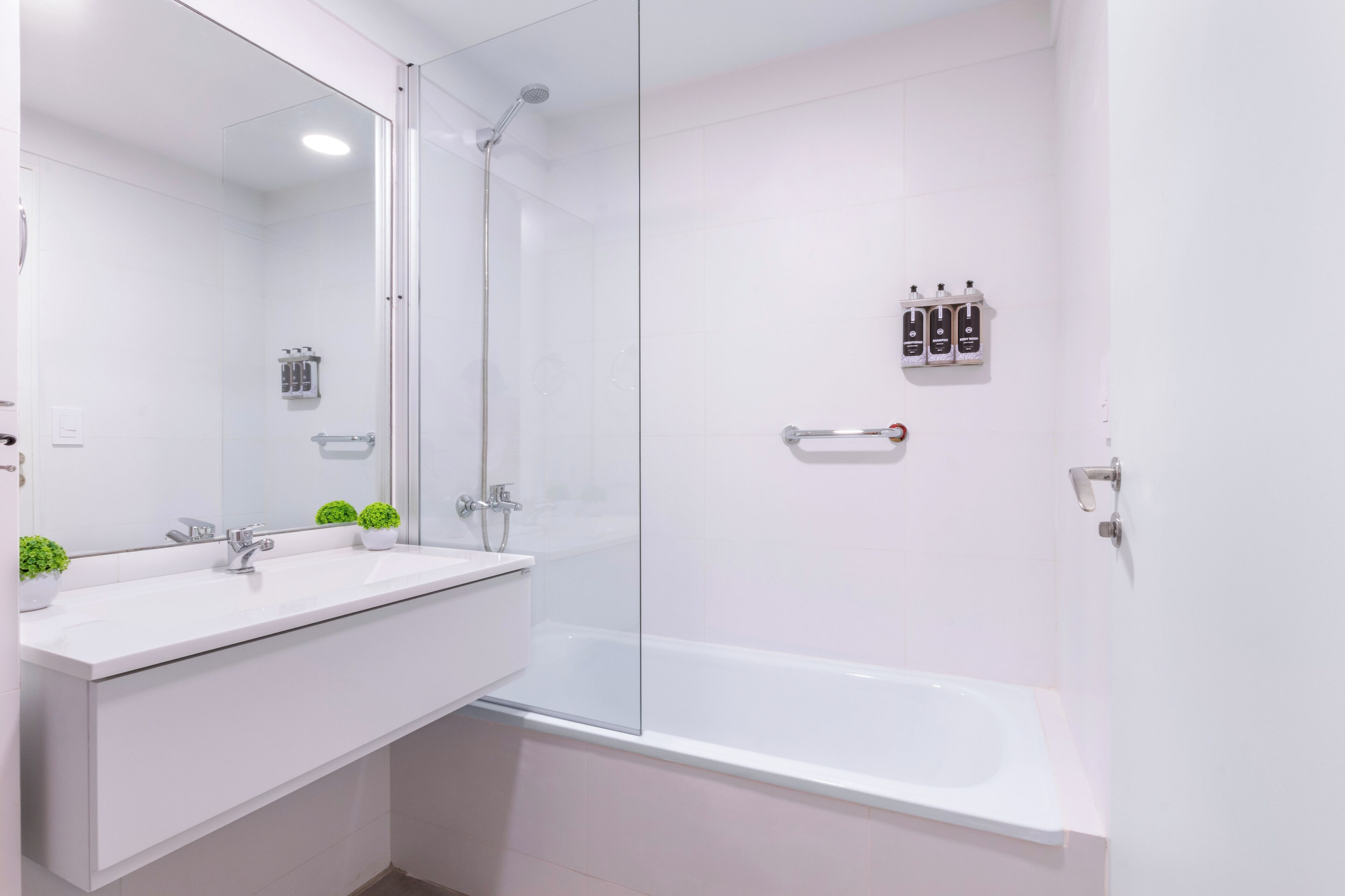 Une salle de bain moderne avec une douche à parois de verre, un lavabo blanc avec un miroir et une baignoire blanche.