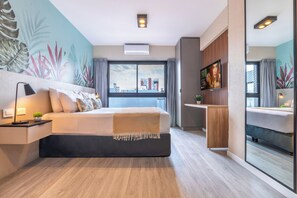 A modern hotel room with a large bed, a bedside table with a lamp, a small plant, a TV, and a large window with curtains. - Deluxe Apartments Downtown by BueRentals (Buenos Aires)