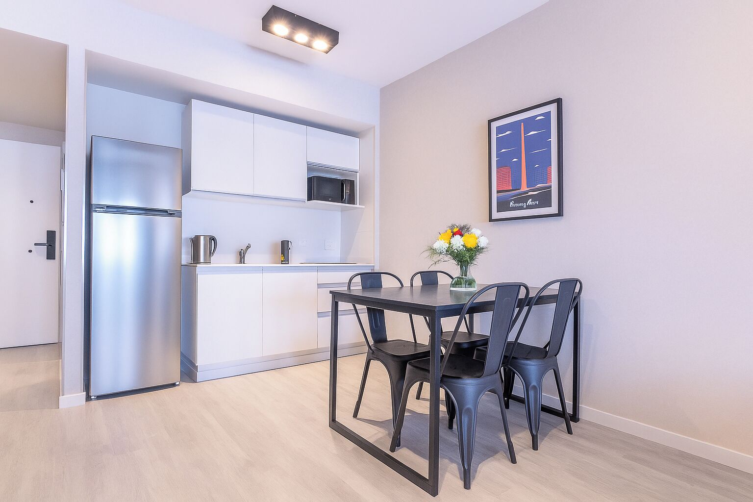 A modern kitchen with white cabinets, a stainless steel refrigerator, and a dining area with a table and chairs.