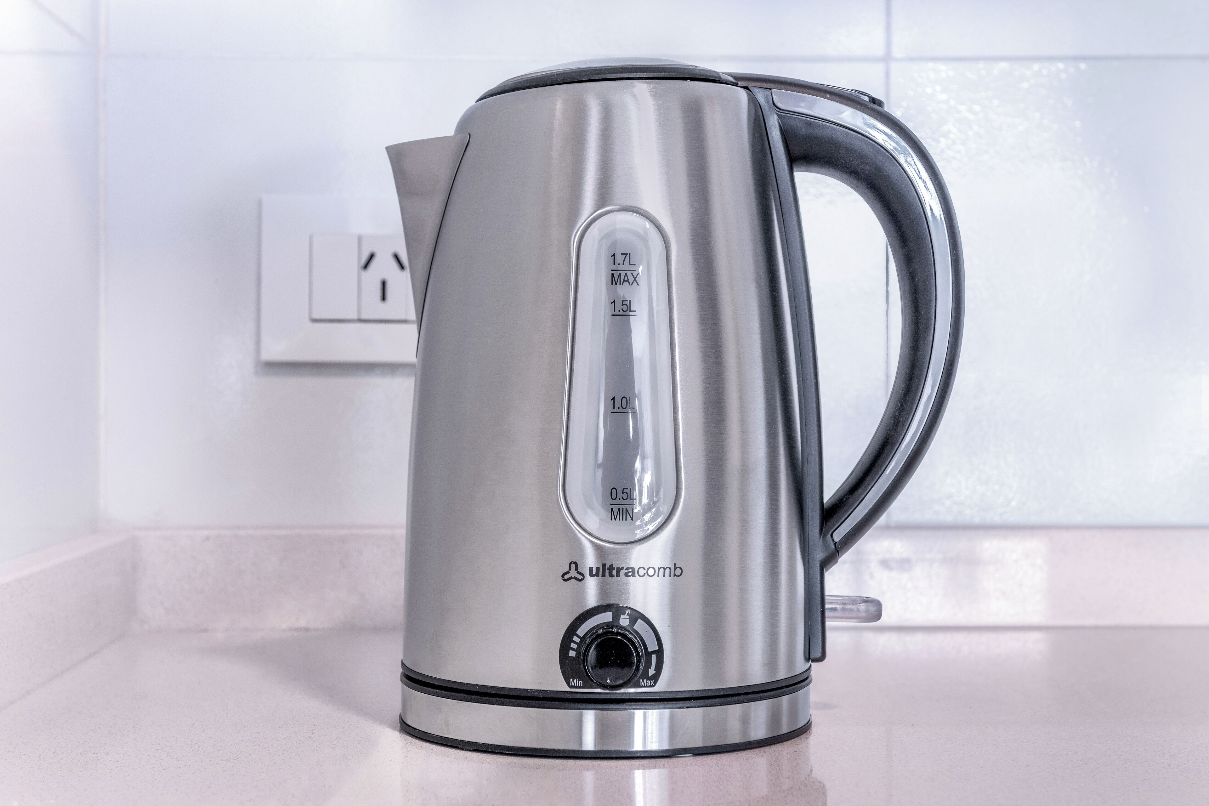 A stainless steel kettle with measurement markings and a brand name on a kitchen counter.