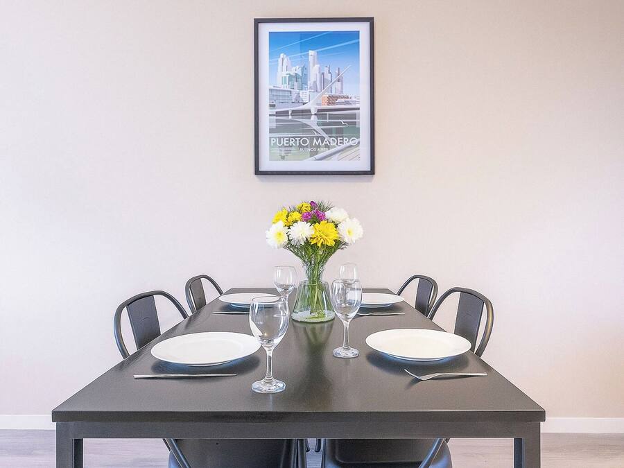 Uma mesa de jantar com quatro cadeiras, um vaso com flores e dois copos de vinho.