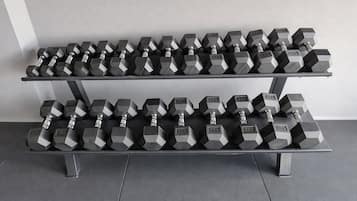 A rack of hexagonal dumbbells with weight markings, arranged on a metal stand against a plain wall.