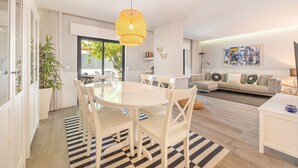 Un salon moderne avec un coin repas, comprenant une grande fenêtre, un ensemble de canapés et un luminaire suspendu.