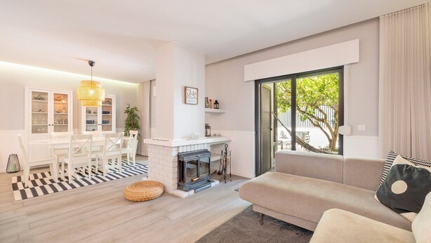 Un salon moderne doté d’une cheminée, d’un canapé, d’un coin repas et d’une grande fenêtre offrant une vue sur la verdure.
