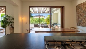 Une cuisine moderne équipée d’une cuisinière à gaz, un coin repas avec une table et des chaises, et une vue sur l’extérieur grâce à une porte vitrée.