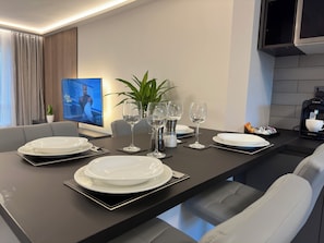 Un comedor moderno con una mesa negra dispuesta para cuatro personas, platos blancos y copas de vino.